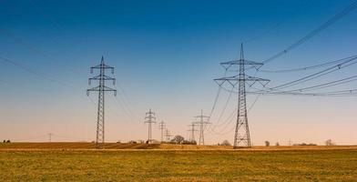 Beautiful farm landscape and high voltage power lines pylons in Germany at Autumn colors during sunset with blue sky. Concept of energy supply and energy crisis. photo