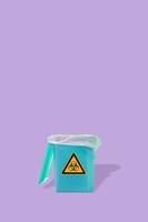 Fluorescent garbage trash bin with its shadows and radiation damger orange symbol isolated at purple solid background. Concept of nuclear waste recycling and environment. photo