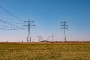 Beautiful farm landscape and high voltage power lines in Germany, at Spring during sunset with blue sky. Concept of energy supply and energy crisis. photo