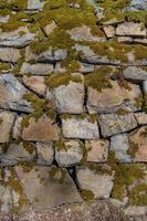 Pattern of ancient bricks and stones at old middle age fortress wall covered with moss, grass and lichen, as a background, closeup, details. photo