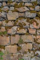Pattern of ancient bricks and stones at old middle age fortress wall covered with moss, grass and lichen, as a background, closeup, details. photo