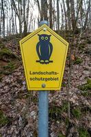 Trail stand post in forest with a sign of an owl bird at yellow background and note that it is protected landscape written in German photo