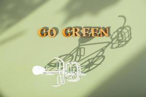 Go green text with bycicle on green background with hard shadows. Sustainable lifestyle concept photo