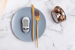 Plate with glucometer and cutlery on plate and alarm clock. Diabetes diet concept photo