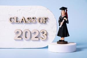 Class of 2023 concept. Wooden number 2023 with graduate statuette on color background photo