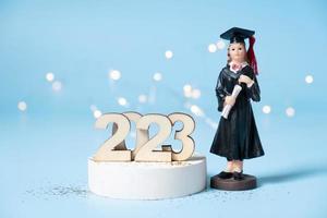 Wooden number 2023 with graduate statuette on color background. Class of 2023 concept photo