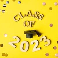 Class of 2023 concept. Wooden number 2023 with graduated cap on yellow background with tinsel photo