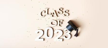 Banner Class of 2023 concept. Wooden number 2023 with graduated cap on beige background photo