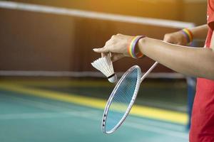 Badminton player wears rainbow wristbands and holding racket and white shuttlecock in front of the net before serving it to player in another side of the court, concept for LGBT people activities. photo