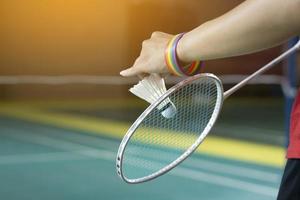 Badminton player wears rainbow wristbands and holding racket and white shuttlecock in front of the net before serving it to player in another side of the court, concept for LGBT people activities. photo