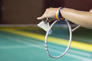 Badminton player wears rainbow wristbands and holding racket and white shuttlecock in front of the net before serving it to player in another side of the court, concept for LGBT people activities. photo