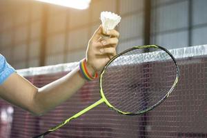 Badminton player wears rainbow wristbands and holding racket and white shuttlecock in front of the net before serving it to player in another side of the court, concept for LGBT people activities. photo