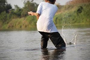 asiático chico es gasto su tiempo libre con amigo por buceo, nadar, lanzamiento rocas y atrapando pescado en el río de local nacional parque juntos felizmente. pasatiempo y felicidad de niños concepto. foto