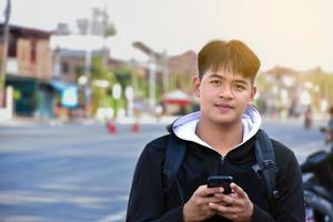 retrato de asiático adolescente chico participación inteligente móvil teléfono y sentado en espalda asiento de moto junto a el rural la carretera en el noche de el día, suave y selectivo enfocar. foto