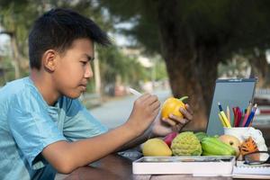 Asian boy holds paintbrush and yellow bell pepper which molded from plaster, coloring and painting outer surface with same color during his free times, idea for hobby and art learning. photo