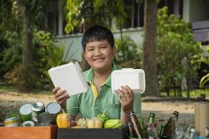 Asian boy is separating garbages and putting them into the boxes in front of him near building, soft and selective focus, environment care, community service and summer vacation activities concept. photo