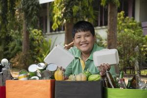 Asian boy is separating garbages and putting them into the boxes in front of him near building, soft and selective focus, environment care, community service and summer vacation activities concept. photo