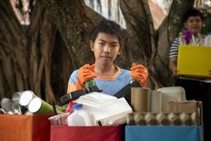 Young asian boy sorting various garbages and putting them into the boxes infront of him in the park, nature care and environment love concept. photo
