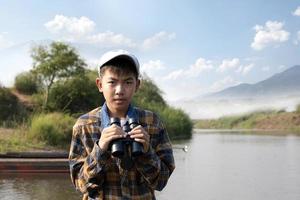 Asian boys using binoculars to do the birdwatching in tropical forest during summer camp, idea for learning creatures, wildlife animals and insects outside the classroom. photo