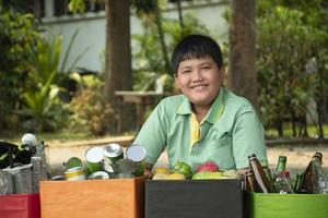 Asian boy is separating garbages and putting them into the boxes in front of him near building, soft and selective focus, environment care, community service and summer vacation activities concept. photo