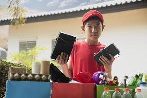 Asian boys are separating garbages and putting them into the boxes in front of them near building, soft and selective focus, environment care, community service and summer vacation activities concept. photo