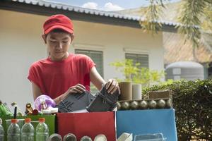 Asian boys are separating garbages and putting them into the boxes in front of them near building, soft and selective focus, environment care, community service and summer vacation activities concept. photo