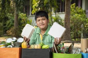 Asian boy is separating garbages and putting them into the boxes in front of him near building, soft and selective focus, environment care, community service and summer vacation activities concept. photo