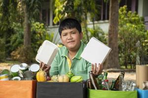 asiático chico es separando basuras y poniendo ellos dentro el cajas en frente de él cerca edificio, suave y selectivo enfocar, ambiente cuidado, comunidad Servicio y verano vacaciones ocupaciones concepto. foto