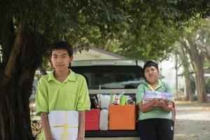 Asian boys are separating garbages and putting them into the boxes in front of them near building, soft and selective focus, environment care, community service and summer vacation activities concept. photo