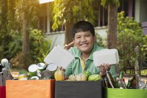 Asian boy is separating garbages and putting them into the boxes in front of him near building, soft and selective focus, environment care, community service and summer vacation activities concept. photo