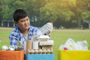 Young asian boy sorting various garbages and putting them into the boxes infront of him in the park, nature care and environment love concept. photo