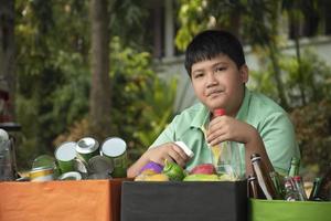 Asian boy is separating garbages and putting them into the boxes in front of him near building, soft and selective focus, environment care, community service and summer vacation activities concept. photo