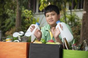 Asian boy is separating garbages and putting them into the boxes in front of him near building, soft and selective focus, environment care, community service and summer vacation activities concept. photo