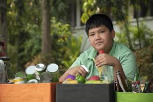 Asian boy is separating garbages and putting them into the boxes in front of him near building, soft and selective focus, environment care, community service and summer vacation activities concept. photo