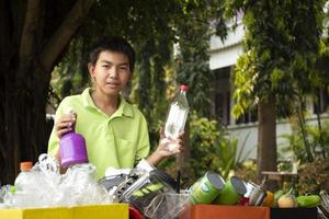 Young asian boy sorting various garbages and putting them into the boxes infront of him in the park, nature care and environment love concept. photo