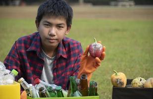 Young asian boy sorting various garbages and putting them into the boxes infront of him in the park, nature care and environment love concept. photo