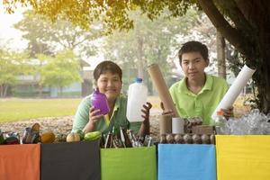 Young asian boy sorting various garbages and putting them into the boxes infront of him in the park, nature care and environment love concept. photo