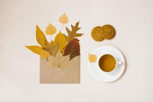 Autumn frame of the flat composition lay on a light background. Fallen leaves in a craft envelope, tea in a cup, oatmeal cookies photo