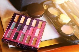 Make-up products and cosmetics with Palette with colorful eyeshadows, Brushes, lipgloss, lipstick on wood table. photo