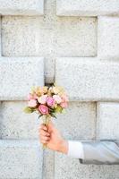 Groom holding a bouquet of pink rose flowers and concrete wall background. Valentine Day for love and celebration Concept. photo
