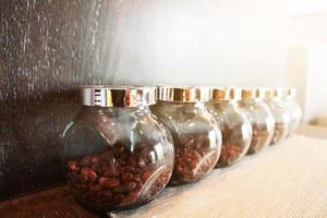 café frijoles en vaso botellas en de madera estante con luz de sol en el cocina.cafe tienda foto
