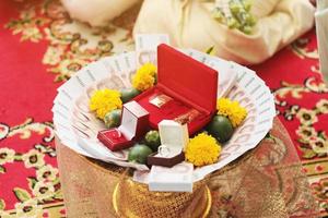 tailandés billetes de banco, oro anillos, verde betel nueces y maravilla flores en bandeja de oro para Boda ceremonia en Tailandia tradicional foto
