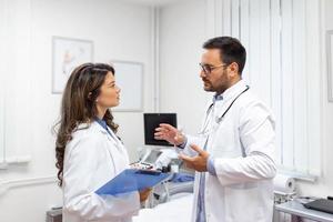 Team of doctors working together on patients file at hospital. Medical staff analyzing report and working at clinic. Woman doctor having discussion in a hospital with colleague photo