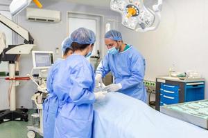 Group of surgeons doing surgery in hospital operating theater. Medical team doing critical operation. Group of surgeons in operating room with surgery equipment. Modern medical background photo