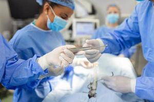 Low Angle Shot in the Operating Room, Assistant Hands out Instruments to Surgeons During Operation. Surgeons Perform Operation. Professional Medical Doctors Performing Surgery. photo