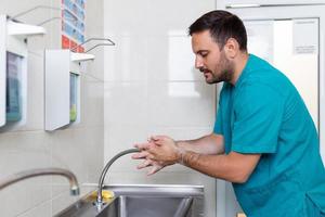 Doctor washing hands with soap. Male surgeon is preparing for surgery. He is in uniform at operating room. photo