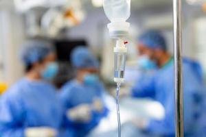 Close-up of IV drip bag in emergency room. Medicine is passing through pipe from intravenous drip. It is in hospital. Surgery in background photo