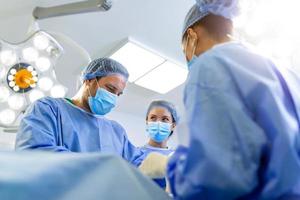 Diverse Team of Professional surgeon, Assistants and Nurses Performing Invasive Surgery on a Patient in the Hospital Operating Room. Surgeons Talk and Use Instruments. Real Modern Hospital. photo