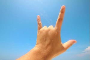 Hand sign of love and showing fingers means I love you on blue sky with sunlight and copty space. photo