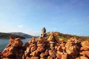 Beautiful Pyramid shape of stones arranged with Buddha statue in zen on rock mountain in seascape of sunset and sea horizon with Dry grass field on Phrom Thep Cape in Phuket island, Thailand. photo